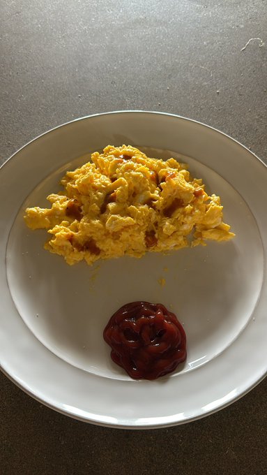 A plate of perfectly cooked scrambled eggs with a dollop of ketchup on the side
