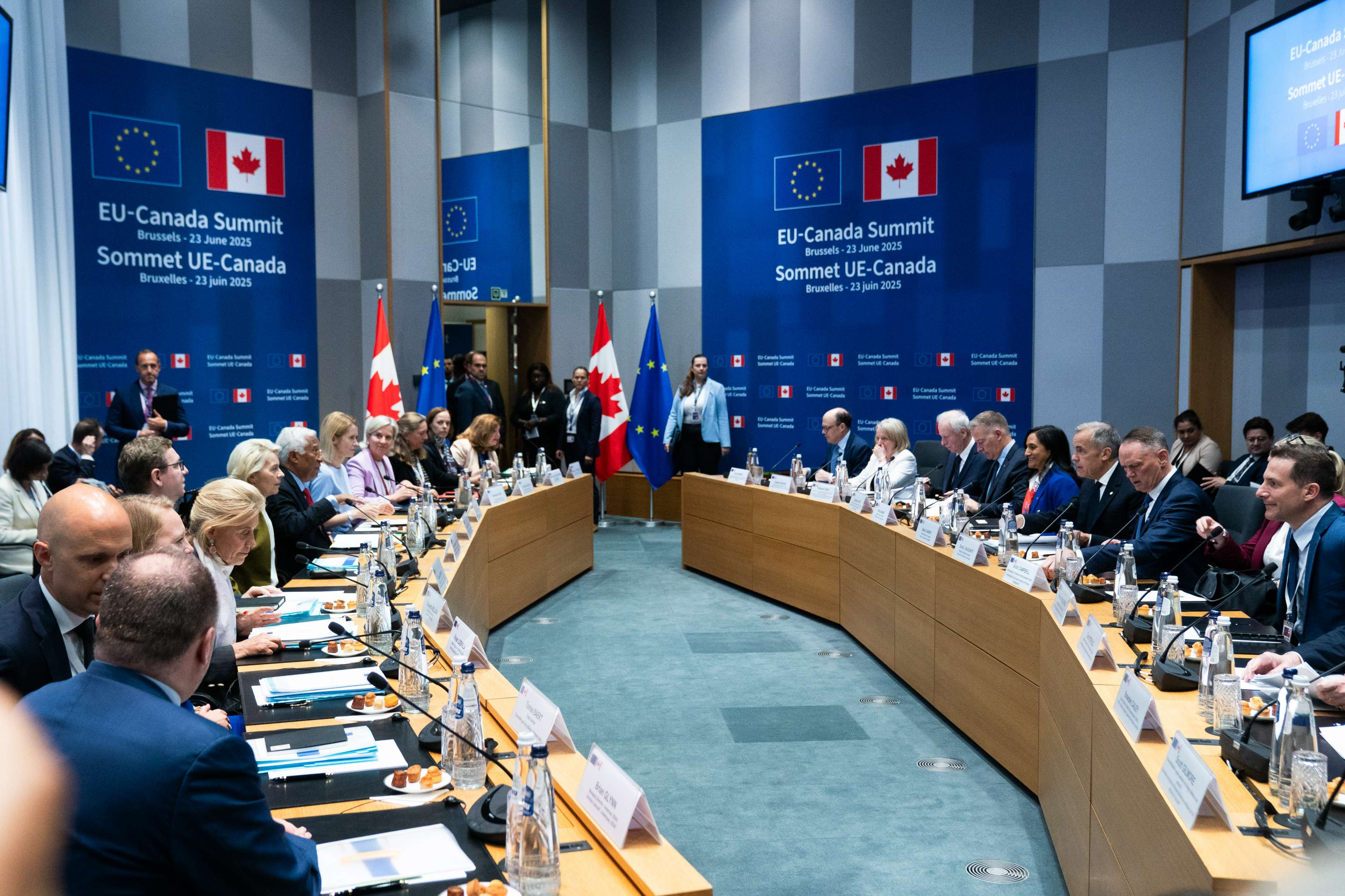 Prime Minister Mark Carney and Canadian officials are seated across from European Commission President Ursula von der Leyen, Vice President Kaja Kallas, and other EU representatives at the Canada–EU Summit. The flags of Canada and Europe are situated in the background.