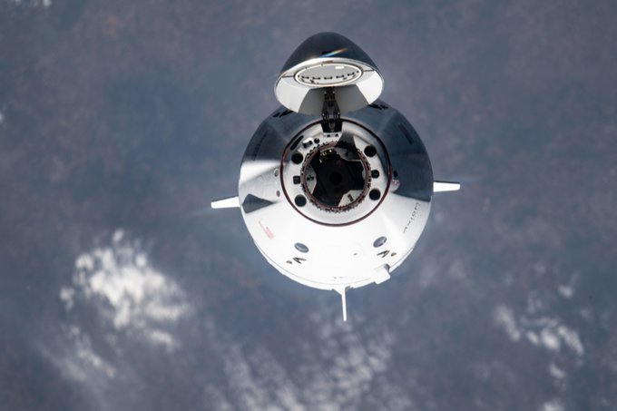A SpaceX Dragon spacecraft approaches the International Space Station. Its conical top is open, with the hatch inside facing the camera. Earth fills the background. Credit: NASA