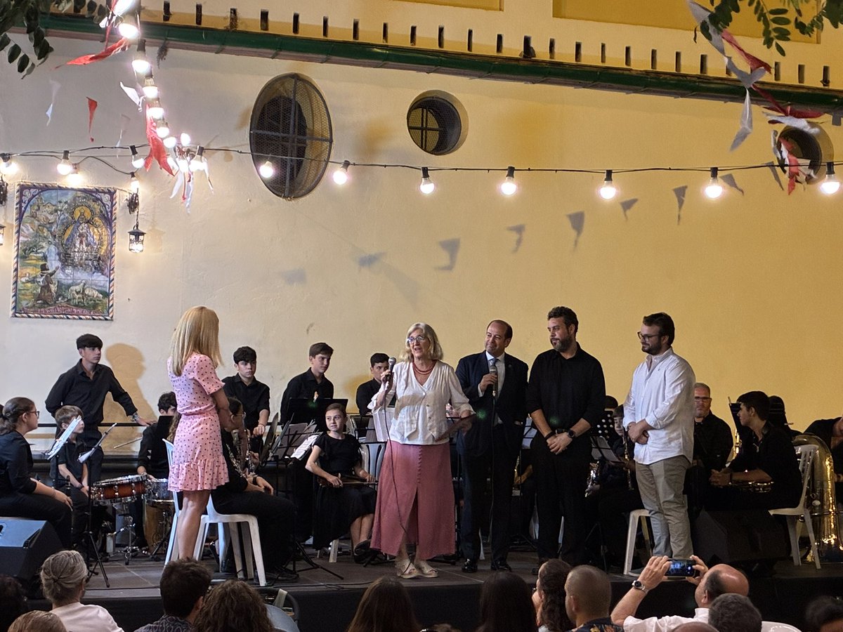 Finaliza su actuación la Banda Juvenil del <a href="/CarmenDSalteras/">El Carmen de Salteras</a>, la cual nos ha deleitado con sevillanas y pasodobles.

La delegada del <a href="/DtoCascoAntiguo/">Distrito Casco Antiguo (Sevilla)</a>, <a href="/amideanr/">Amidea Navarro</a>, entrega un recuerdo a nuestra querida Banda del Carmen.

A continuación, actuará la academia de baile de Alicia Vega.