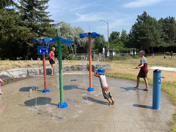 Two young children and an adult play at a City of Ottawa Splash Pad.