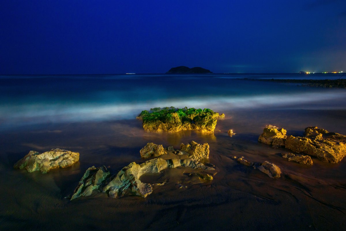 HainanToday's tweet image. Night falls over the bay in Wanning, Hainan. Scattered rocks rest quietly as waves drift in like mist, brushing the shoreline. In the distance, faint lights shimmer like stars falling into the sea.
#seaview #Hainan #travel #nature