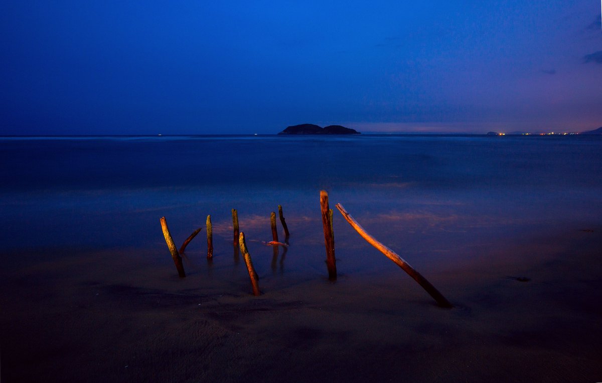 HainanToday's tweet image. Night falls over the bay in Wanning, Hainan. Scattered rocks rest quietly as waves drift in like mist, brushing the shoreline. In the distance, faint lights shimmer like stars falling into the sea.
#seaview #Hainan #travel #nature