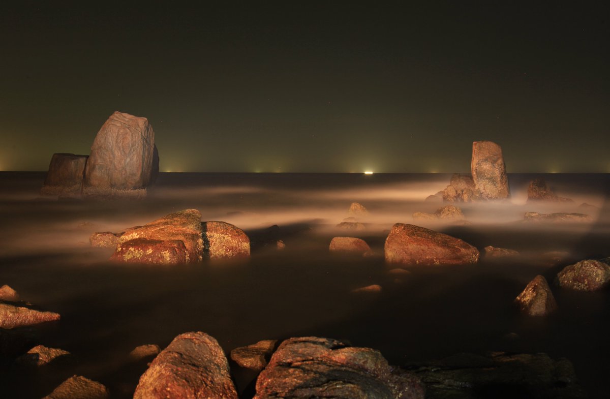 HainanToday's tweet image. Night falls over the bay in Wanning, Hainan. Scattered rocks rest quietly as waves drift in like mist, brushing the shoreline. In the distance, faint lights shimmer like stars falling into the sea.
#seaview #Hainan #travel #nature