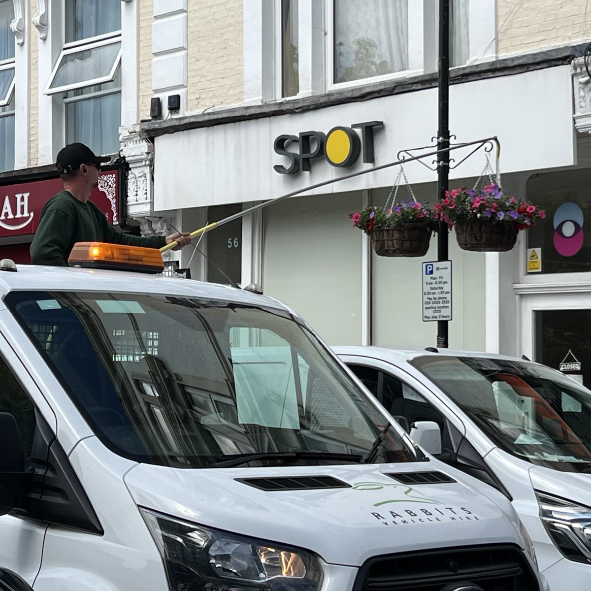 Guy in the back of a truck with a water tank and extension hose…just rolling down the street watering all the flower baskets like it’s a normal thing.