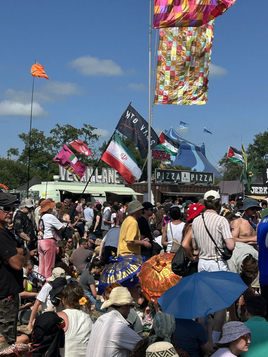 Nothing says peace and love like the flag of the Islamic Republic of Iran flying next to a vegan food truck as thousands gather to cheer Kneecap, whose member has been charged with a terror offence. Just another afternoon at Glastonbury!