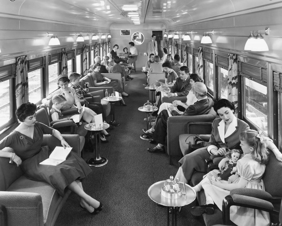 HistoryGirlBW's tweet image. A stunning 1950s photo that captures the golden age of rail travel in exquisite detail. Elegant decor, plush seats, wall mounted lamps and curtains. Passengers immersing themselves in books, drinks, and conversation.
