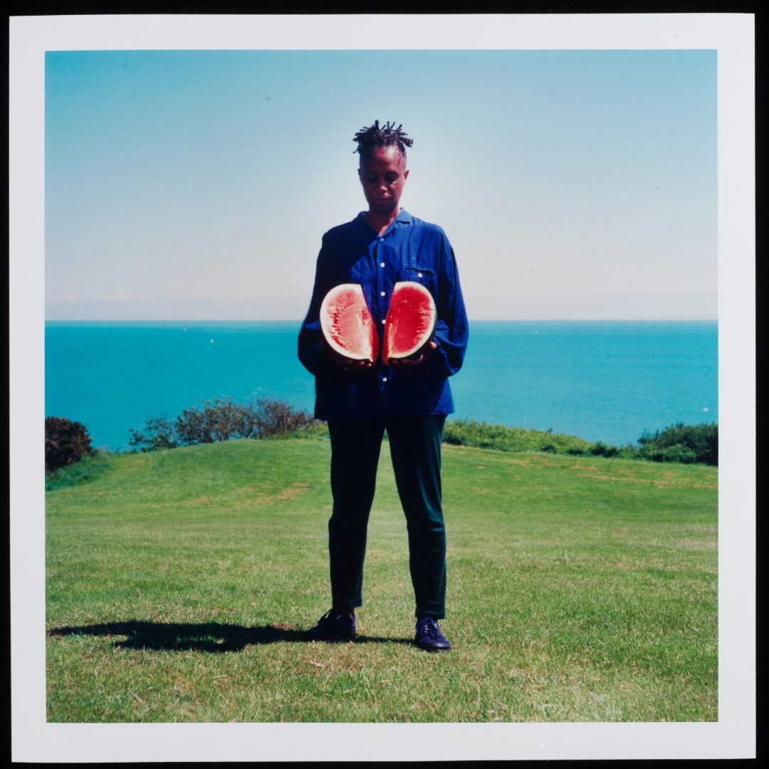 V_and_A's tweet image. Ingrid Pollard, pioneering Black British photographer and ABP founder, challenges cultural stereotypes in her Self-Evident series. Portraits of black men and women in the English countryside, each holding objects linked to the Afro-Caribbean diaspora.