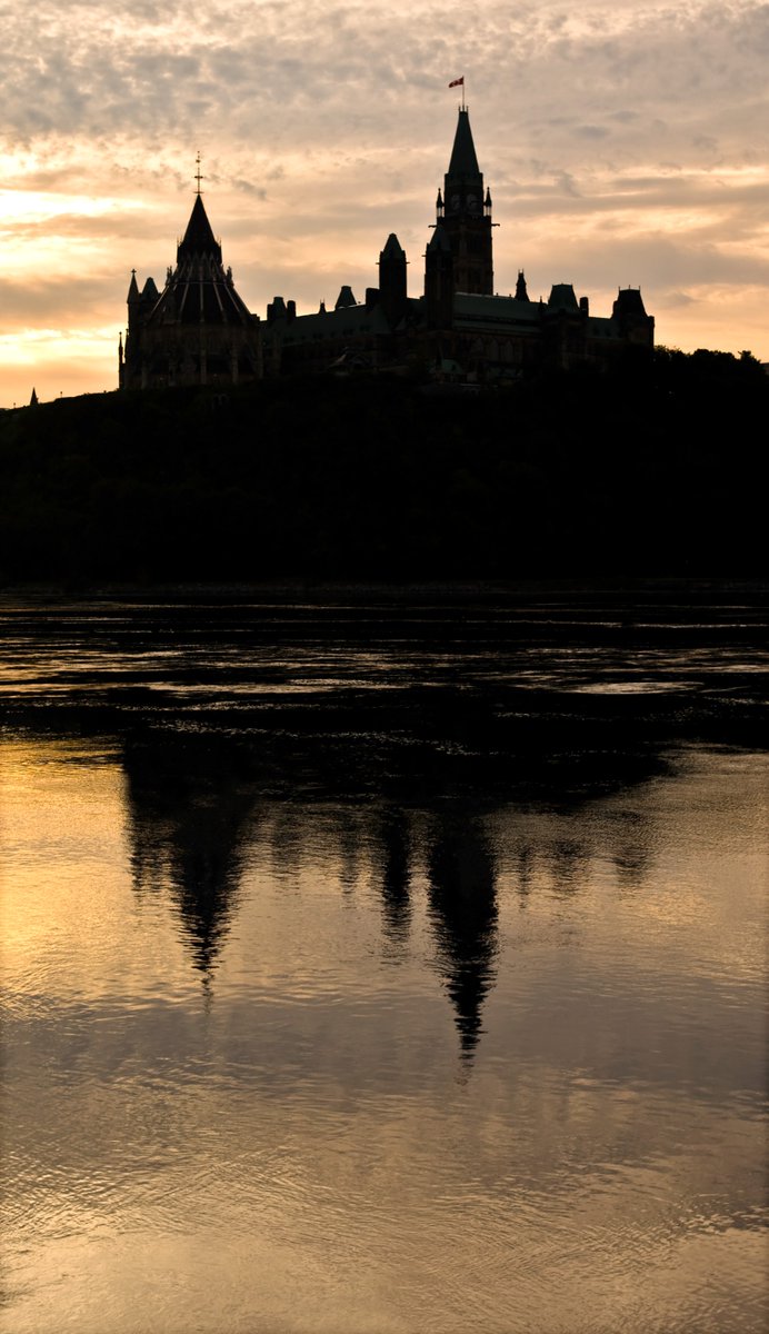OurCommons's tweet image. Parliament silhouetted against the setting sun, reflecting in the Ottawa river during a long summer evening.