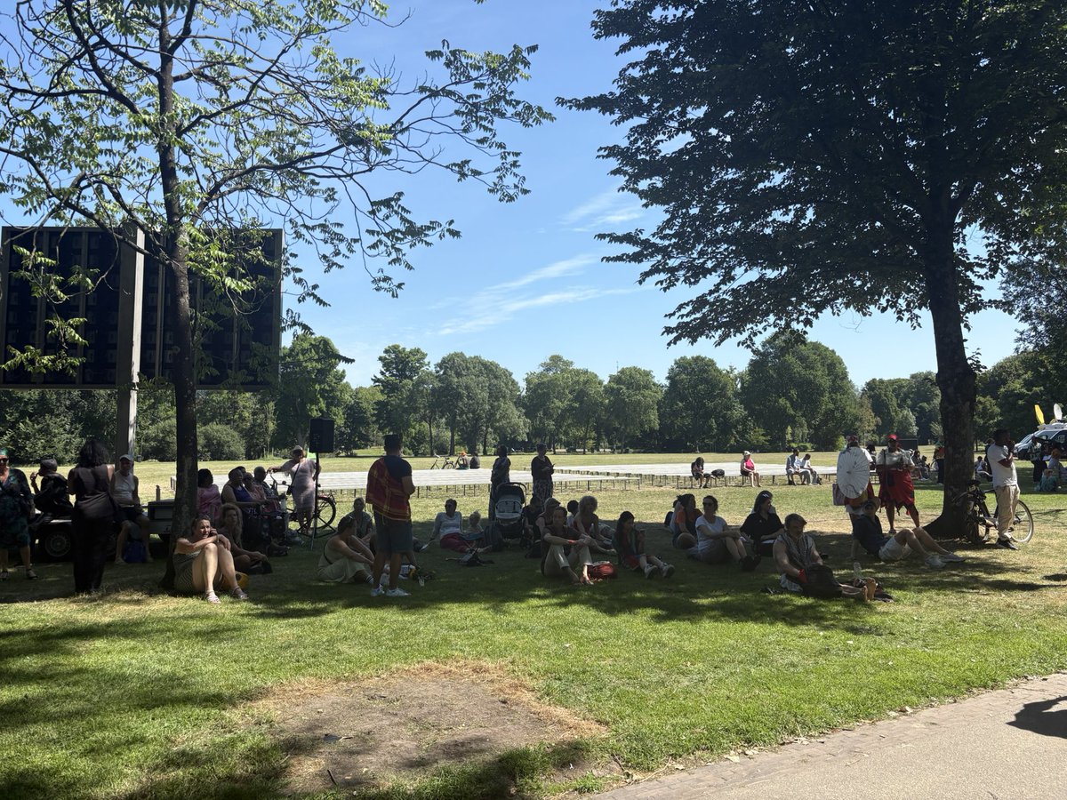 Ondanks de hitte is het lekker druk bij de #ketikoti herdenking in het Oosterpark. De bankjes voor publiek zijn alleen niet heel handig geplaatst: in de volle zon. Dan liever staan of in het gras zitten in de schaduw
