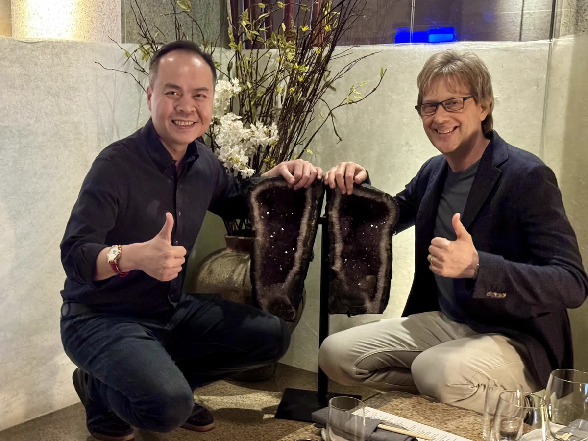 Jack Huynh and Mark Cerny side by side, smiling and giving thumbs up, each touching a piece of amethyst split from the same stone — symbolizing their friendship and the co-engineered partnership behind Project Amethyst.