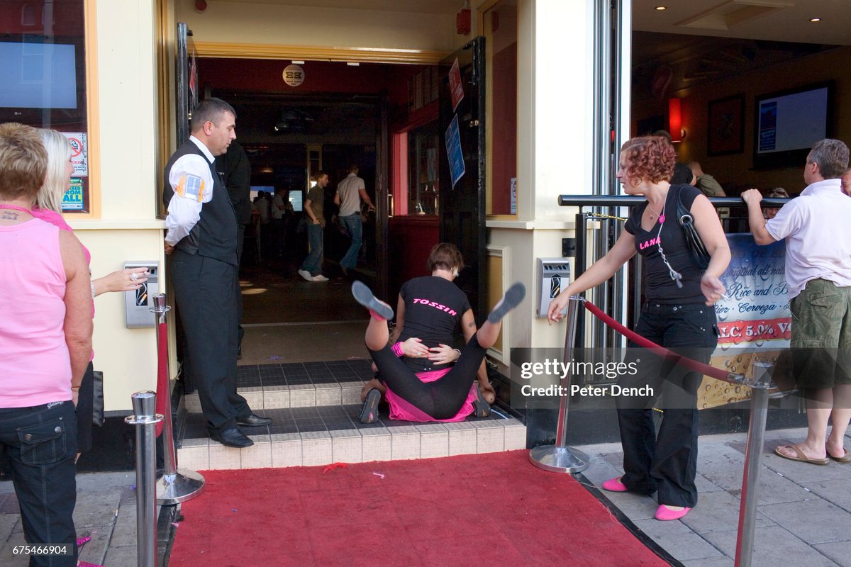 shitbritishpics's tweet image. A door security man watches two women out in Blackpool with a hen party fool about on the floor of Nellie Deans Piano Bar on the North Promenade (2008)