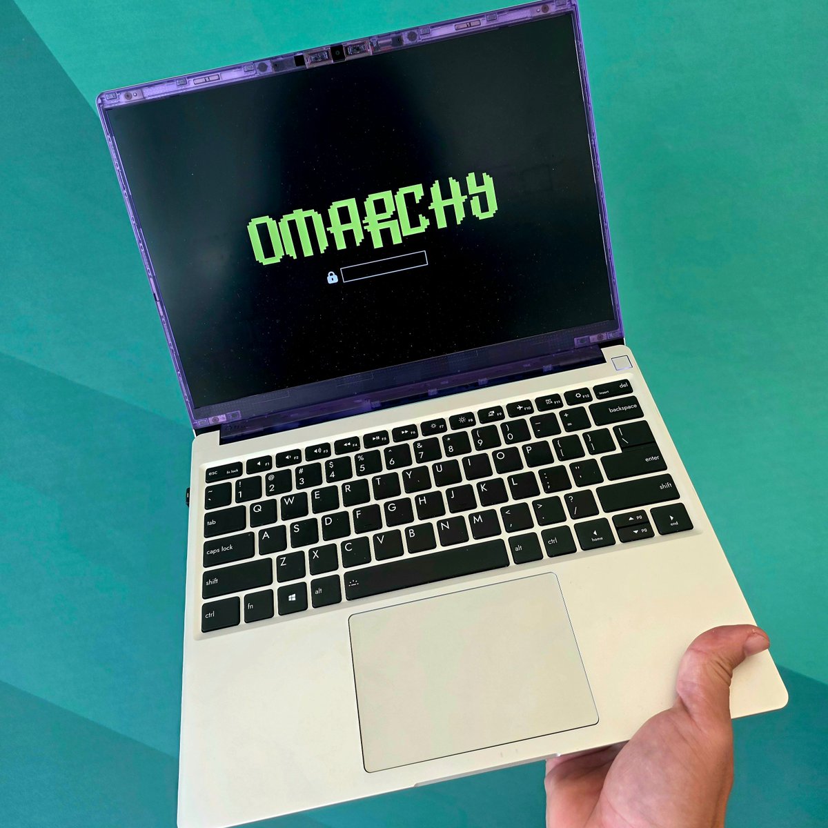 dhh's tweet image. Just got this purple translucent display cover for the @FrameworkPuter 13. Love the retro vibes together with the new Omarchy decryption boot screen 🤩