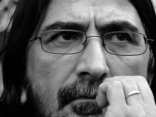 Sene 2010 bir konser için geldiğimiz Ankara’nın işlek caddelerinden birinde oturduk, arkadaşlarımla kahve içiyoruz. Bir an sokakta sakin ve mert adımlarla yürüyen bir adam gördüm. Kirli sakalı Ankara’nın beton rüzgarını adeta zımparalıyordu. Bedeni zayıftı ama asla çelimsiz