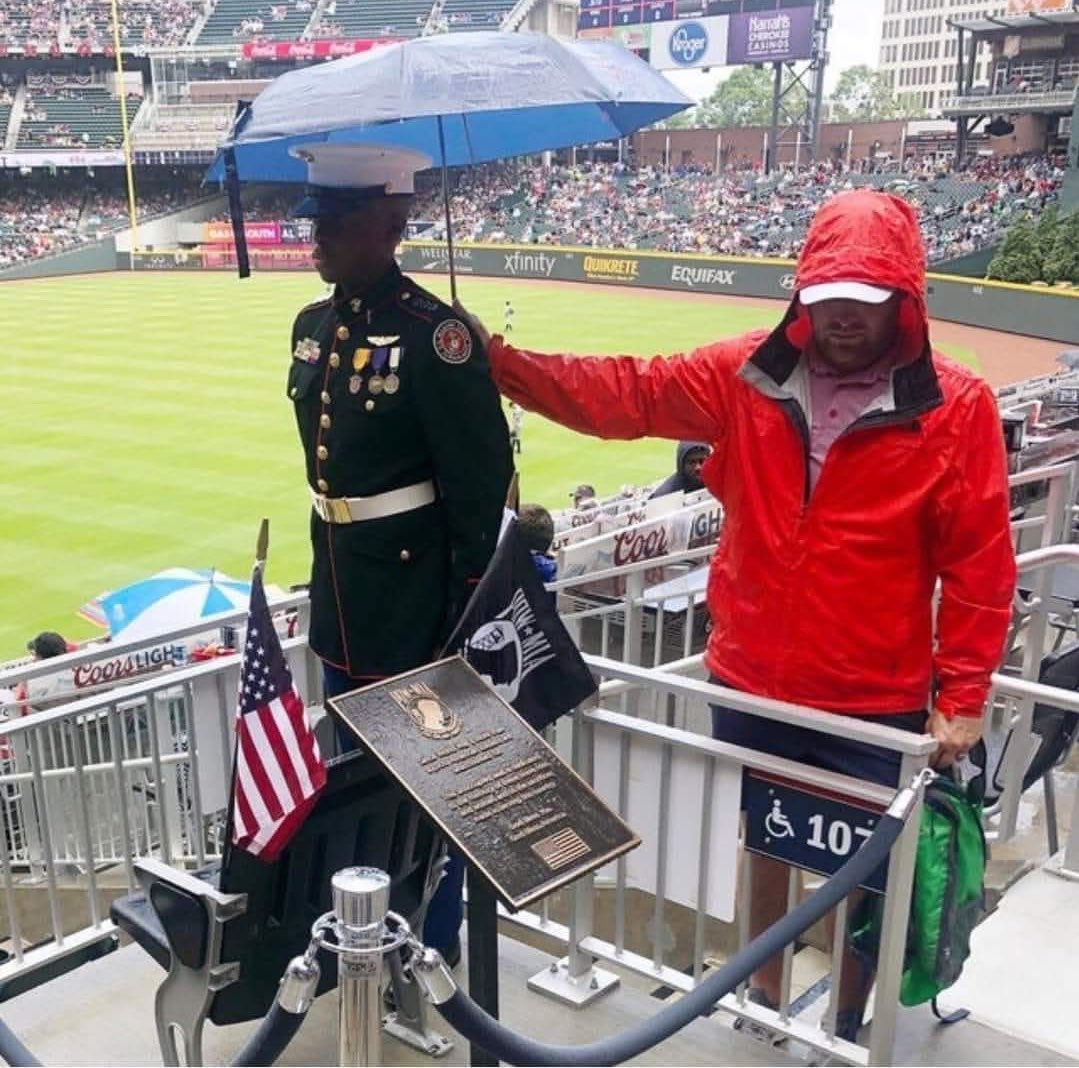 This gentleman holding an umbrella over a marine standing by the seat and plaque dedicated to the 92,000+ unaccounted American soldiers since WWII
