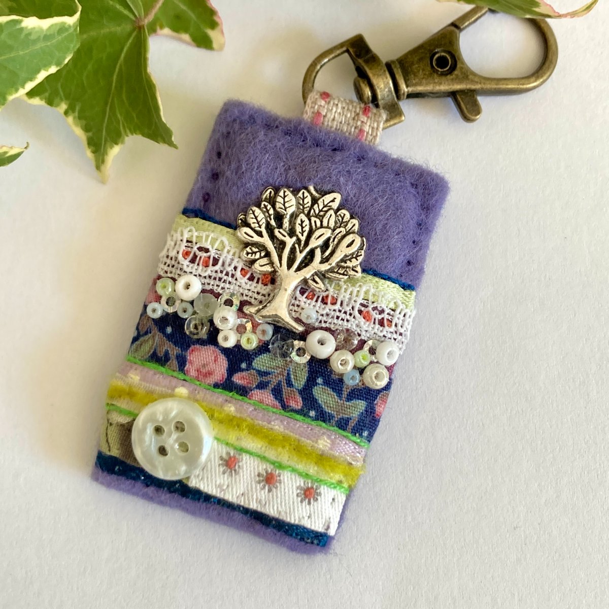 Pretty tree themed clip accessory, designed to attach to bags, keys and spiral-bound notebook journals. Sewn by hand from lavender mauve felt and decorated with layers of mixed fabrics, trims, embellishments and stitching.
elliestreasures.square.site/product/tree-c…

#shopindie #UKGiftAM #giftideas
