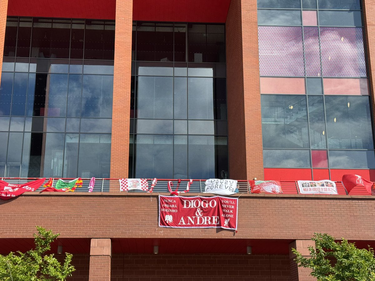 JamesPearceLFC's tweet image. Tributes to Diogo Jota and his brother Andre Silva now cover the entire length of the Main Stand and beyond, from Anfield Road to Walton Breck Road. Flowers, scarves, shirts, hats, flags, banners, even PlayStation controllers. 
An outpouring of love and grief.