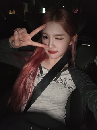 Rohaona's tweet photo. the image captured in a dimly lit car, her striking pink hair cascading over her shoulders, glowing softly against the dark interior, her casual yet stylish outfit, a grey shirt with delicate patterns peeking out from a dark sleeve, paired with the seatbelt snug across her chest. https://t.co/G7vYMSK7tG