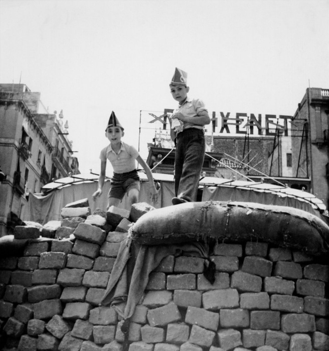 Another one by Gerda Taro. Two kids dressed up as militia fighters  mucking about on a barricade in front of El Molino, El Parallel. Barcelona, August 1936. Advert for Freixenet cava behind.