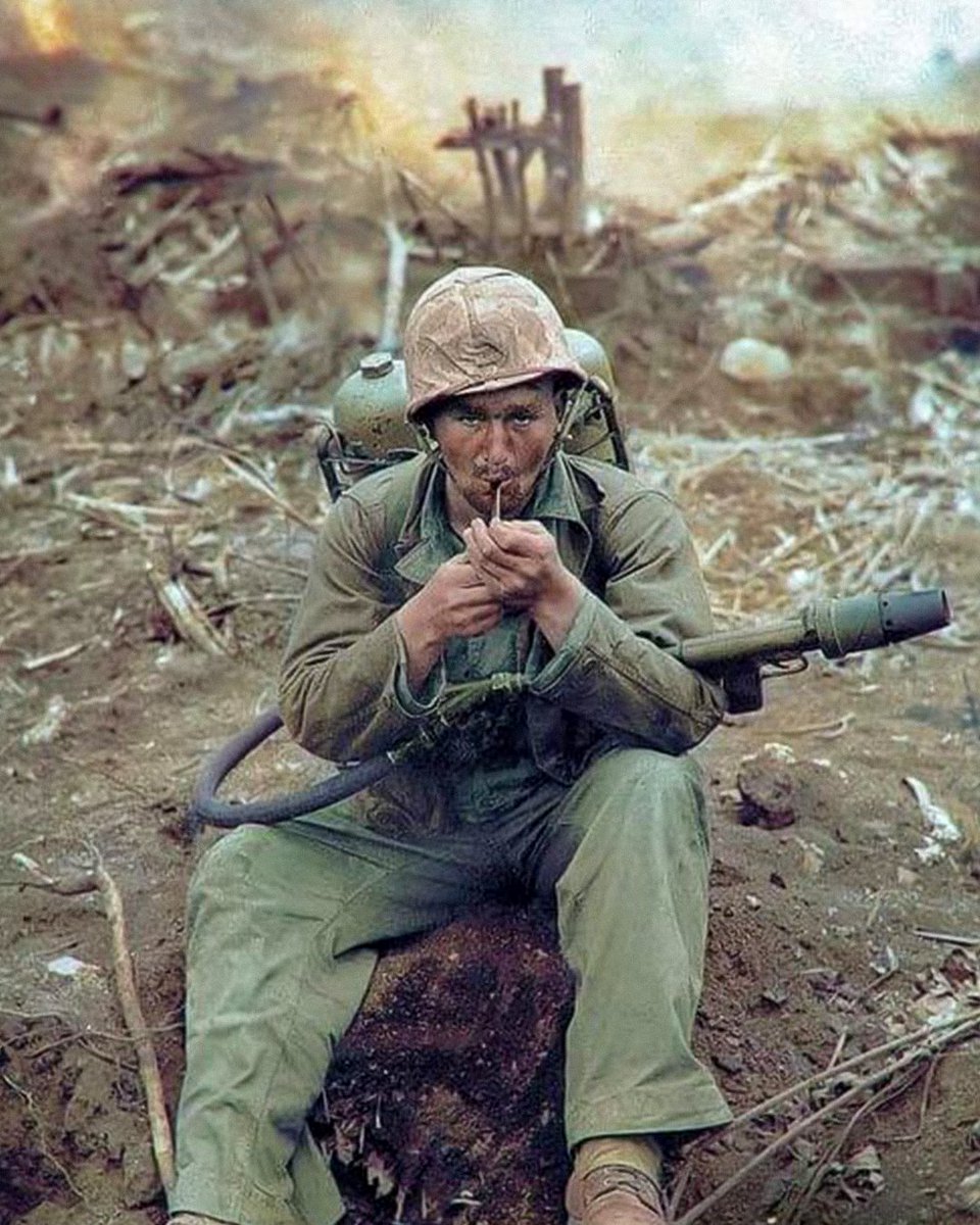 NationalVMM's tweet image. A young U.S. Marine sits amid the devastated battlefield of Iwo Jima in 1945, calmly lighting a pipe, with a flamethrower strapped to his back.
#historicalphoto #wwii #worldwarii #pacifictheater #usmc #semperfi