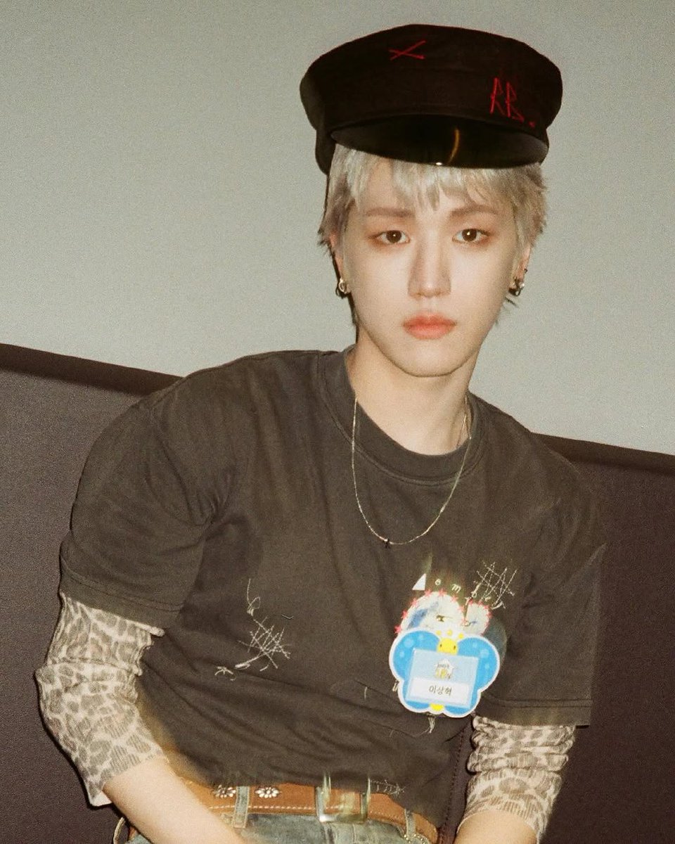 The monochrome hat, slightly askew, hints at rebellious flair, while the layered leopard sleeves beneath the graphic tee add a touch of untamed spirit. A delicate chain necklace and artful accessories seal the ensemble with understated sophistication.