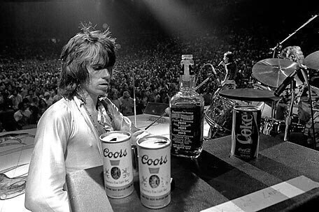 Keith Richards with a bottle of Jack Daniels, Two Coors, and a Coke at a concert, 1972. Photo by Ethan Russell
