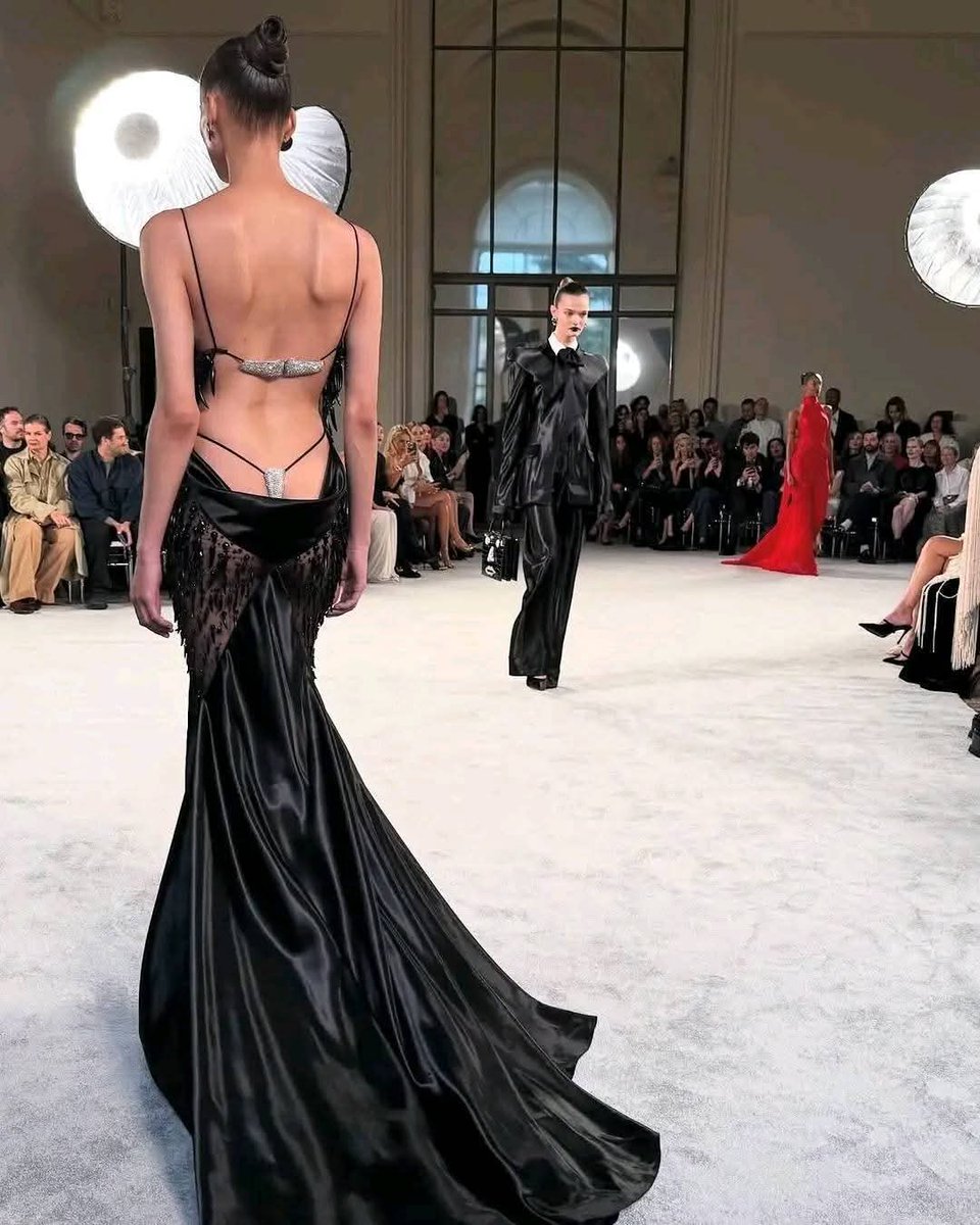 davincimag's tweet photo. #Schiaparelli Fall couture 2025 worn by Annemary Aderibigbe.
 Wearing a sleeveless bias-cut dress in flowing satin, enhanced with a corset top and transparent tulle panels embroidered with horn-shaped elements on the sides of the dress, and a silver rhinestone jewelled thong https://t.co/xsnQBvWog2