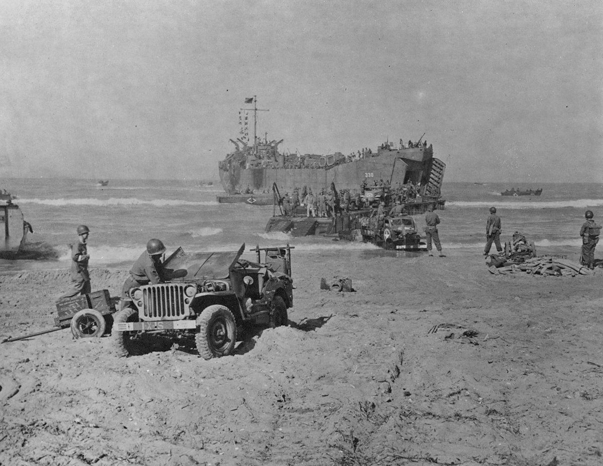 LST unloading vehicles and supplies on the beach in Gela, Sicily, Italy, Jul 1943; note Ford GPW Jeep in foreground