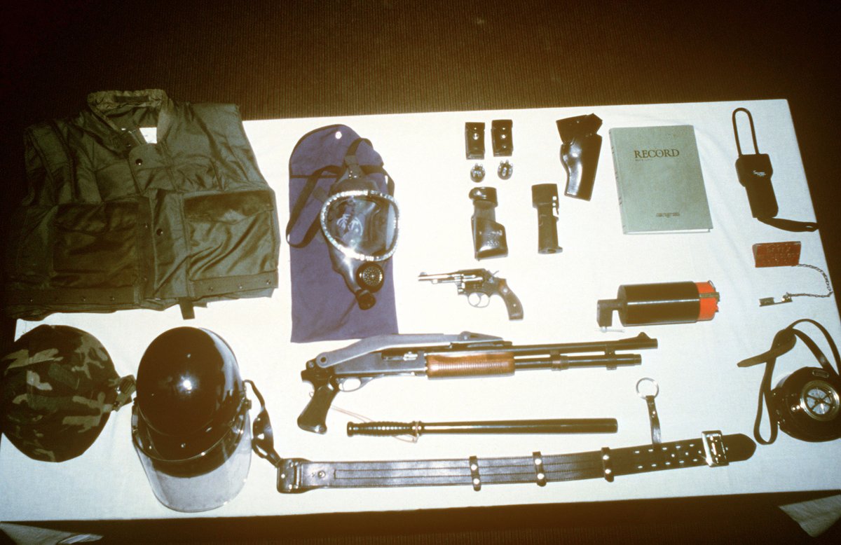 Marine Corps riot control gear arrayed for inspection. Among the equipment displayed are a gas mask, protective vest, riot shotgun, .38-caliber revolver, nightstick and logbook.