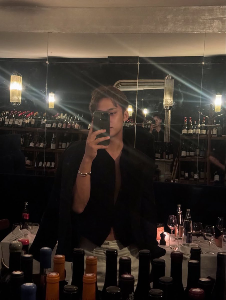 KimMingzyu's tweet photo. Took this shot while the night was still young and the vibe was right. I kept the look simple—a black top, white pants, and a few bracelets to finish it off. The wine bottles behind me and the soft glow from the lights gave it a solid backdrop, nothing too flashy, just clean. https://t.co/BJR7uvwsnq