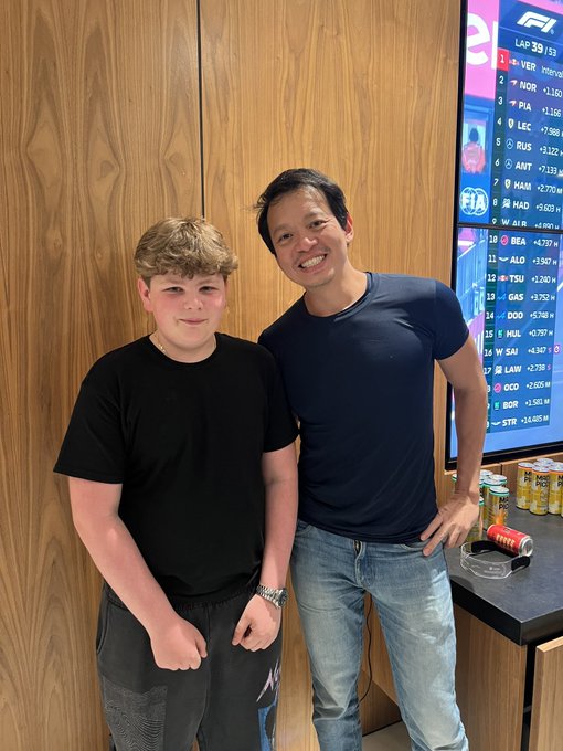Hayden and Mark Davis standing together in front of a wooden wall and a digital leaderboard