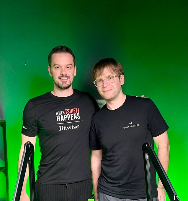 Evgeny Gaevoy and Kevin WSH posing together in front of a green screen, wearing branded t-shirts