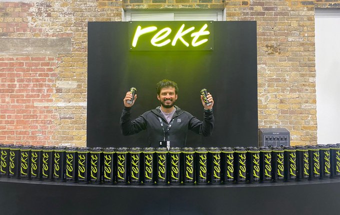 Rektのロゴと大量の缶が並ぶディスプレイの前でRekt Drinksの缶を持つ人