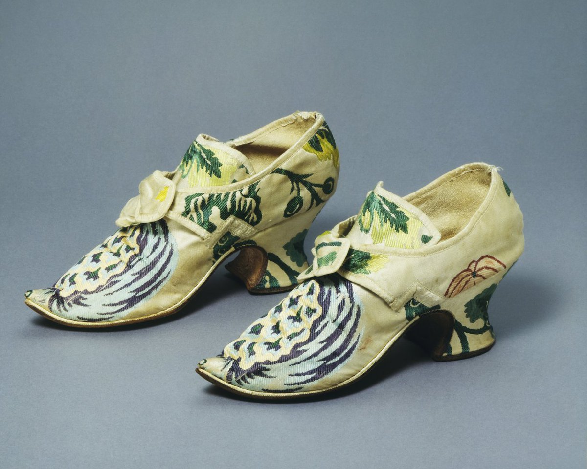 V_and_A's tweet image. Silk footwear in the 18th century reflected elegance and status. Women’s shoes featured curved heels, pointed toes, and silk uppers with detailed floral motifs. Intended for indoor use only, they fastened with cut steel buckles. Outdoor wear required practical leather boots.