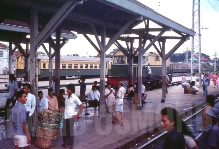 Foto karya Railfan David Osmond ini langka karena jarang lokomotif KAI difoto tanpa plat nomor dan logo. Lokomotif BB 303 ini difoto di Stasiun Manggarai, Jakarta pada 1976. Pada masa itu penumpang yang membawa barang pikulan masih lazim ditemui di stasiun - stasiun kota besar.