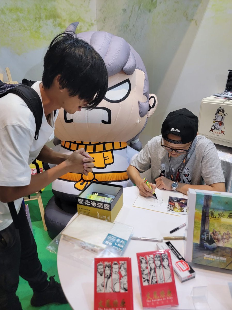 RoT_eng's tweet image. 🎉 || The Facebook account has shared pictures of Chan Mou and some of his illustrations at the signing event - and he’s even wearing one of the new Eight Geniuses shirts that debuted at the Book Fair!