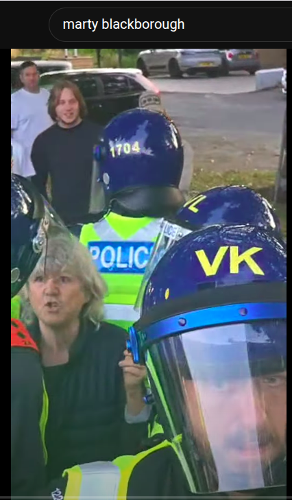 PHandwright's tweet photo. #Epping #Esses was peaceful for hours.

This woman showed up and began remonstrating with protestors, a couple of dozen cops had to escort her away.

If you went into the middle of a free palestine demo you'd be arrested, she gets an escort from @EssexPoliceUK #TwoTierPolicing https://t.co/Nh9Bjn1kAm