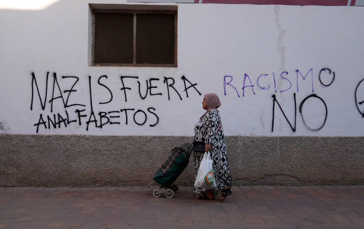 Una mujer camina junto a una pintada en una calle del barrio de San Antonio, en Torre Pacheco. Foto: ALFONSO DURAN/ EL PAÍS