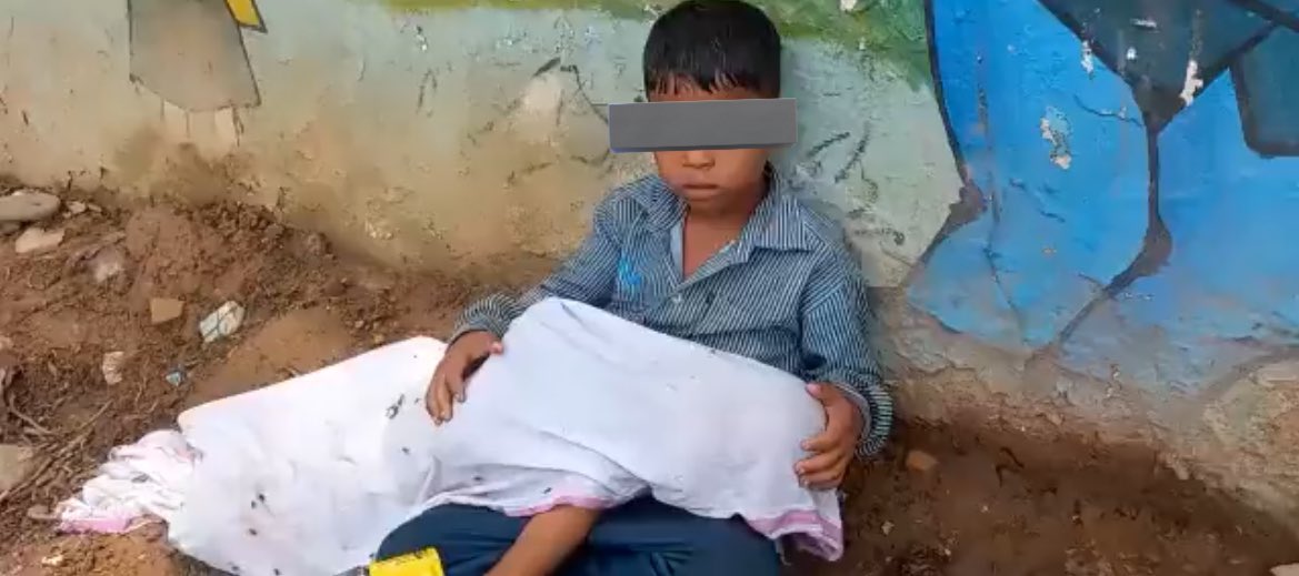 Yea ek purani tasveer hai jaha 8 saal ka bacha apne 2 saal ke chote bhai ki laash ko apni godi me rakh kar betha hai kyunki aspatal ne keh diya tha ki khud bache ki laash le kar jao. In bachon ke pita ambulance dhundne gye thae aur bache ki laash par makhiya bhin bina rahi thi.