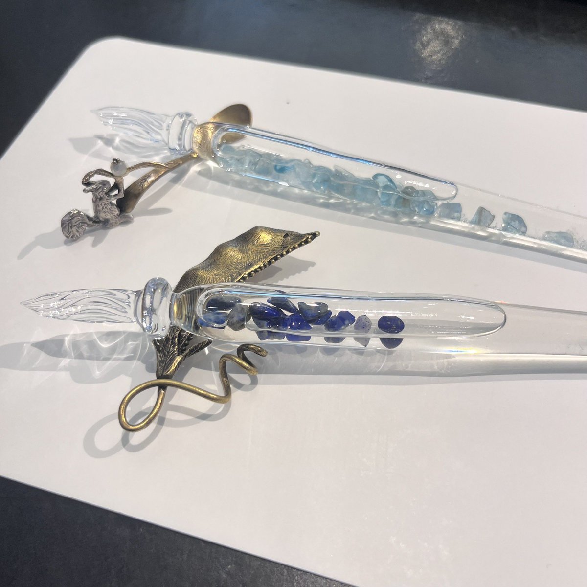 DT_stylo's tweet image. まつぼっくりのガラスペンのご紹介
上がアパタイト、下がラピスラズリのストーン、一緒に入っているストームグラスは気温によって表情を変えます。
ペンレストは佐々木ひとみさんの作品。
また7/26(土)にはまつぼっくりオリジナルガラスペン受注会を開催。お好きなストーンでガラスペンが作れます。