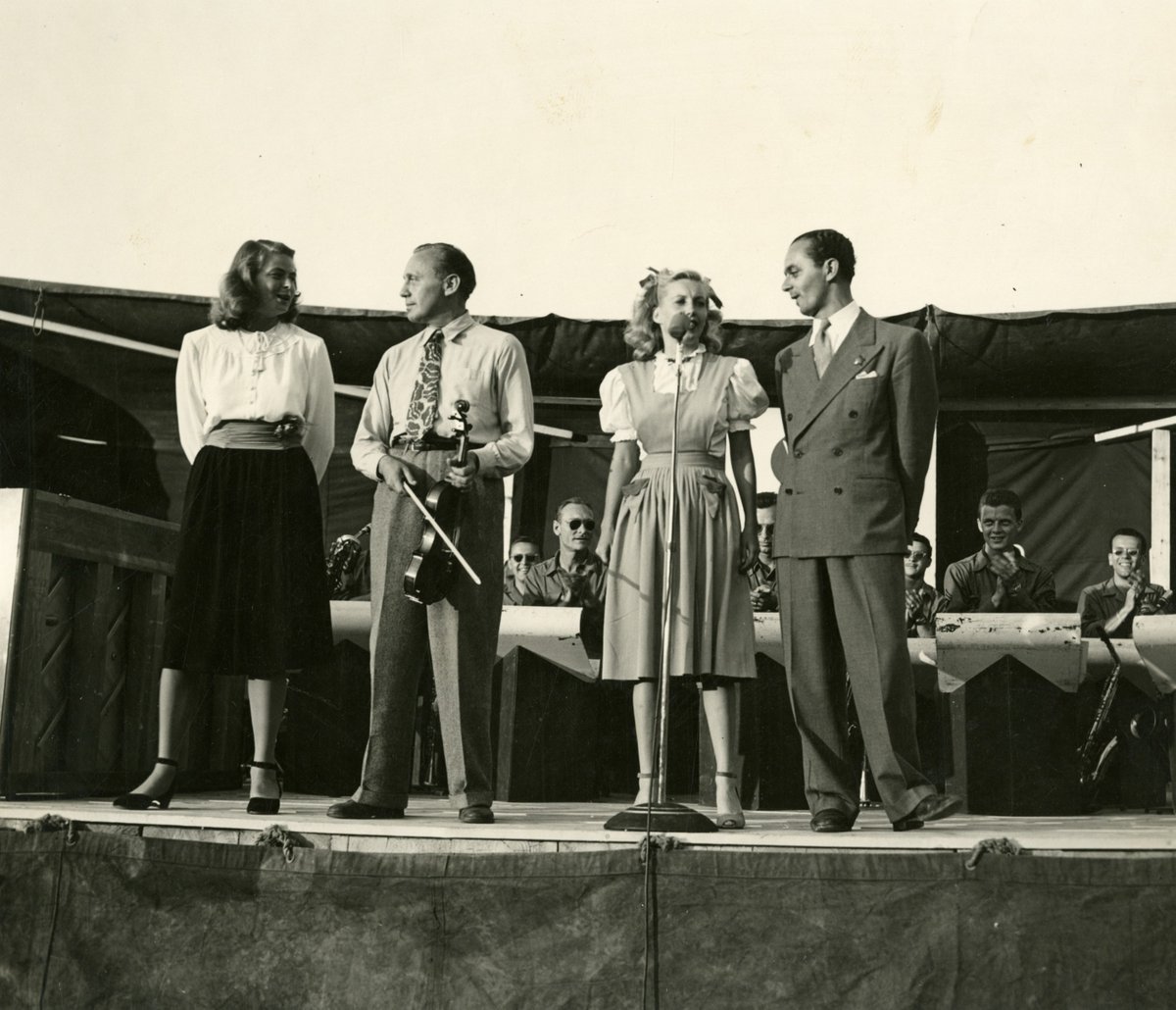 In this image from the Museum's Digital Collections taken July 24, 1945, Hollywood entertainers Ingrid Bergman, Jack Benny, Martha Tilton, and Larry Adler sing together during a USO performance in Germany.