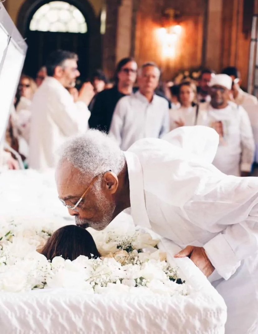 Jaqueloureco's tweet image. Um pai beijando a testa da filha em seu último adeus. A dor que rompe a ordem natural da vida. Enterrar um filho é sepultar parte de si.
 #PretaGil