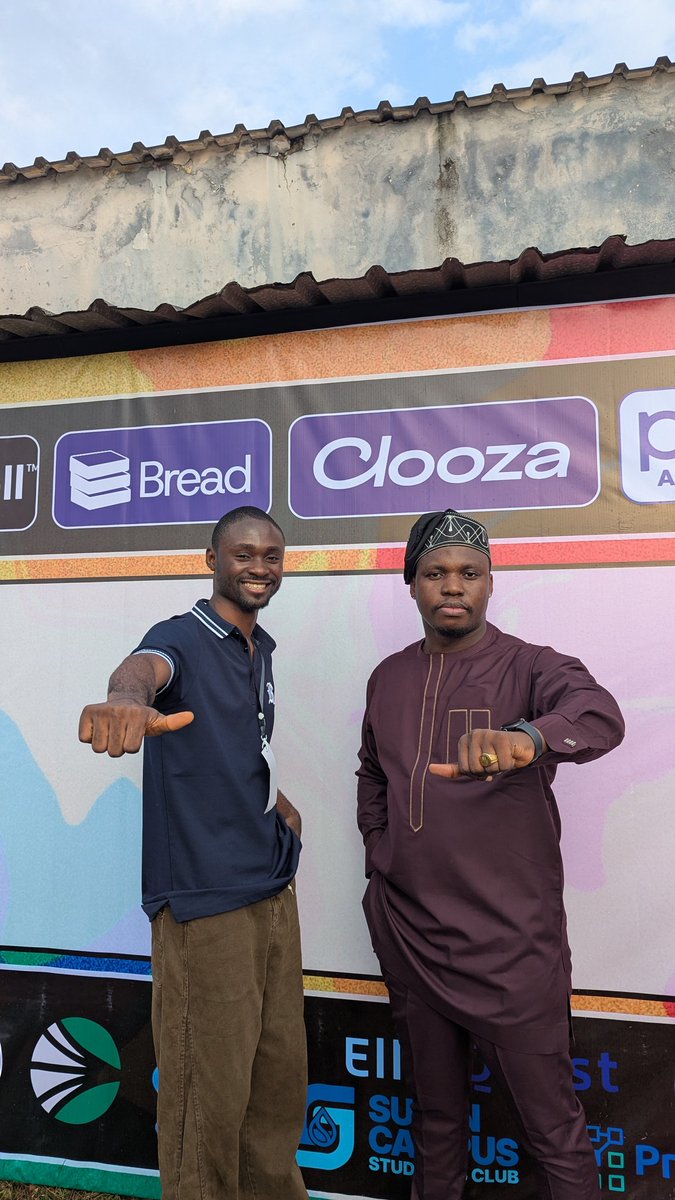 Two individuals posing and pointing at the camera in front of a banner with blockchain company logos