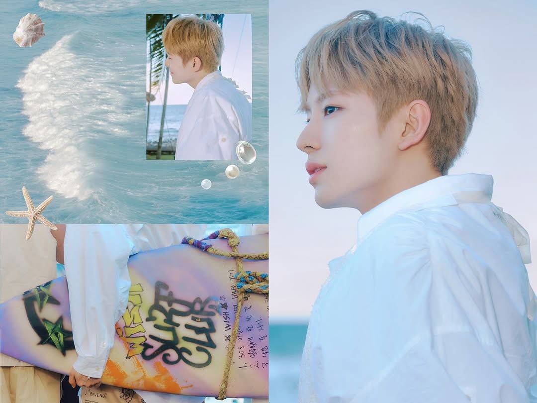 Standing by the ocean, wind in my hair, wearing a white shirt, holding a colorful surfboard with graffiti art. The waves crash behind, the sky is soft blue, and everything feels calm. Just taking in the view, hearing the water, feeling the sand.