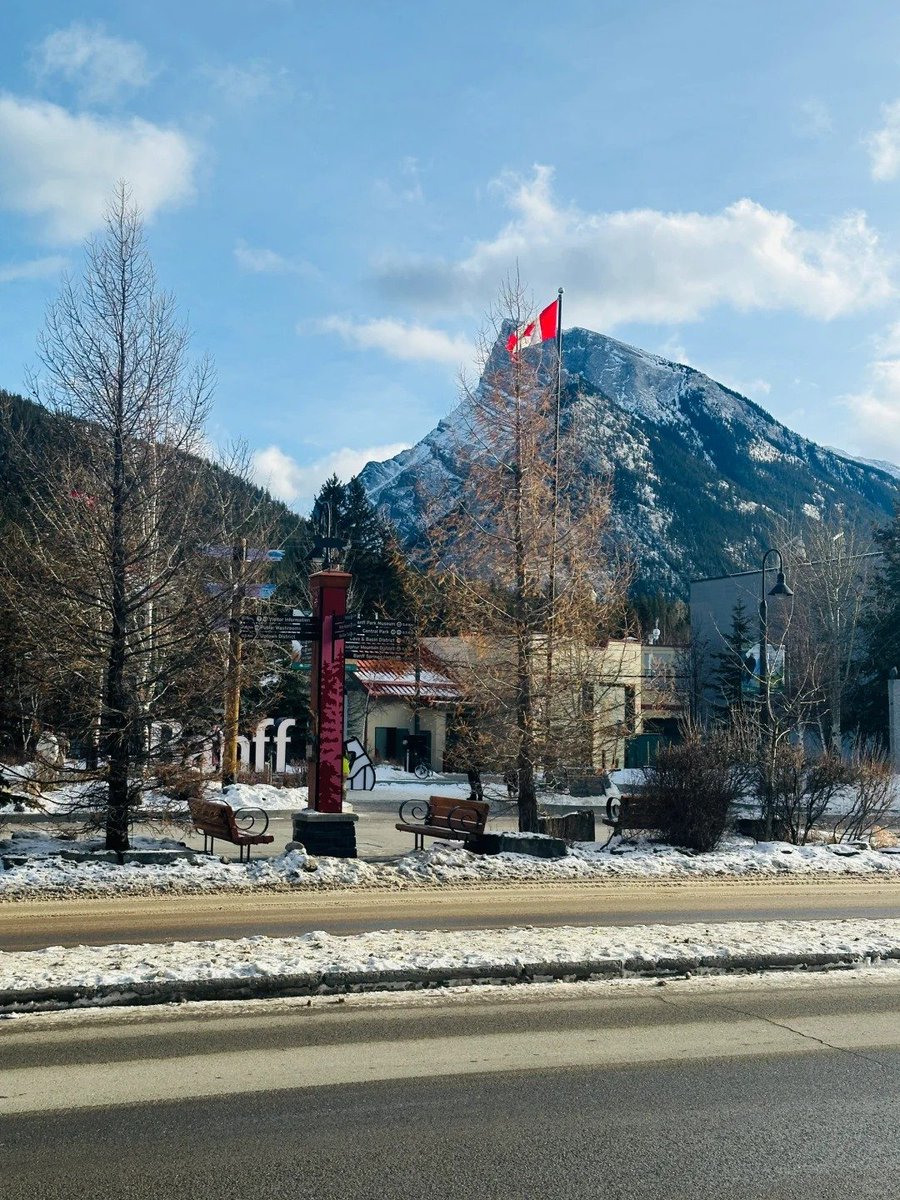 Charming winter vibes in the mountains 🏔️❄️  cozy town streets buzzing with life, all under the majestic gaze of snow capped peaks and the proud Canadian flag 🇨🇦🏘️.