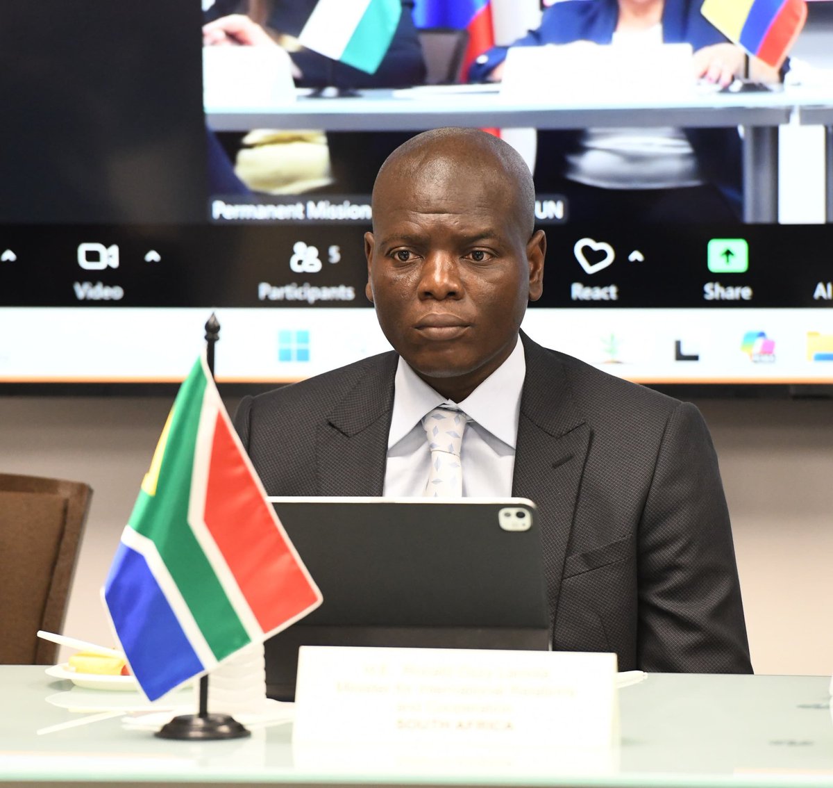 Ronald Lamola seated at desk with South African flag and nameplate during UN engagement.