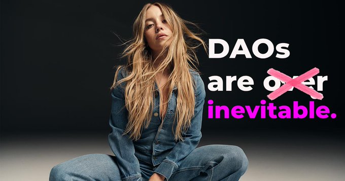 진한 분홍색으로 'over'에 줄이 그어진 'DAOs are over inevitable'라는 문구가 있는 데님 옷을 입은 사람