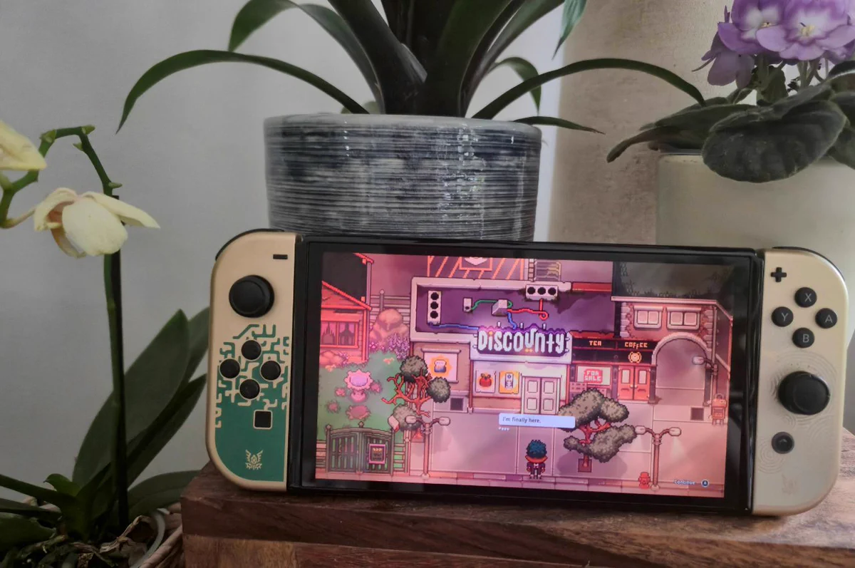 Nintendo Switch OLED playing the Discounty demo. The console is on a wooden table surrounded by potted plants.