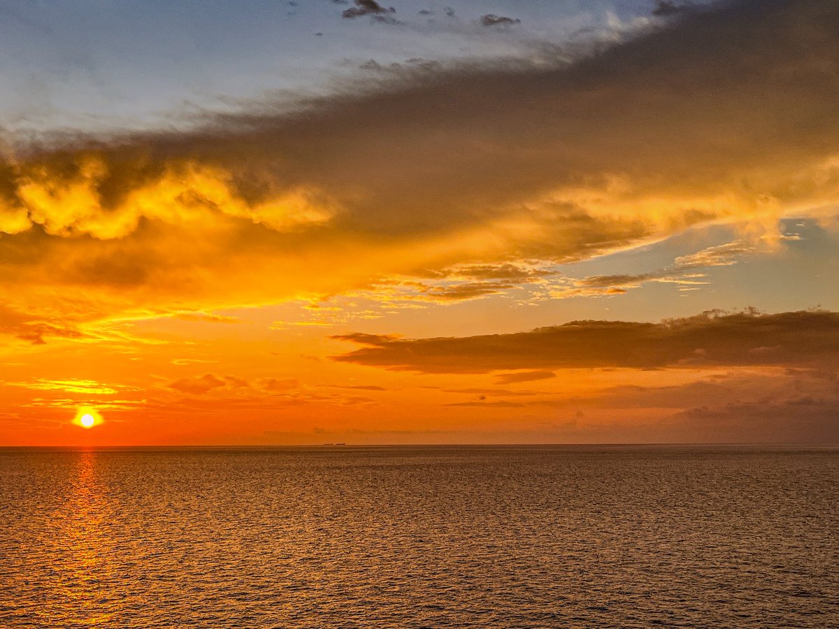 A smile of fire lights up the west,
As ocean rocks the sun to rest.
Each ripple glows, a soft reply,
To secrets shared between sea and sky.