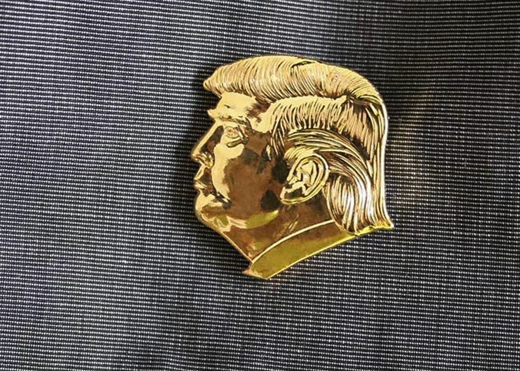 This is a lapel pin in Trump's likeness. Many of his cabinet members are wearing them them instead of the American flag. They say they weren't forced to wear them.